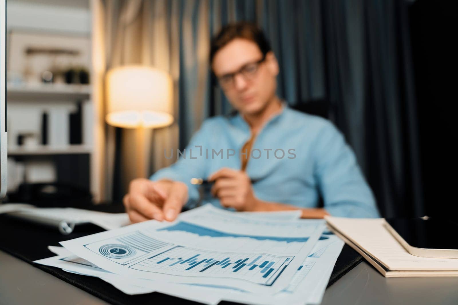 Smart businessman holding paperwork report paragraph dynamic database, looking at pc screen with analyzing global target evaluation value profit company at modern home office at night time. Pecuniary.