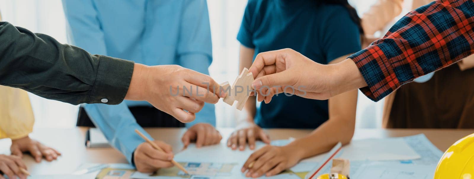 A cropped image of architect cooperate with engineer to build house during engineer team draft the blueprint on table with architectural equipment scatter around. Focus on hand. Delineation.