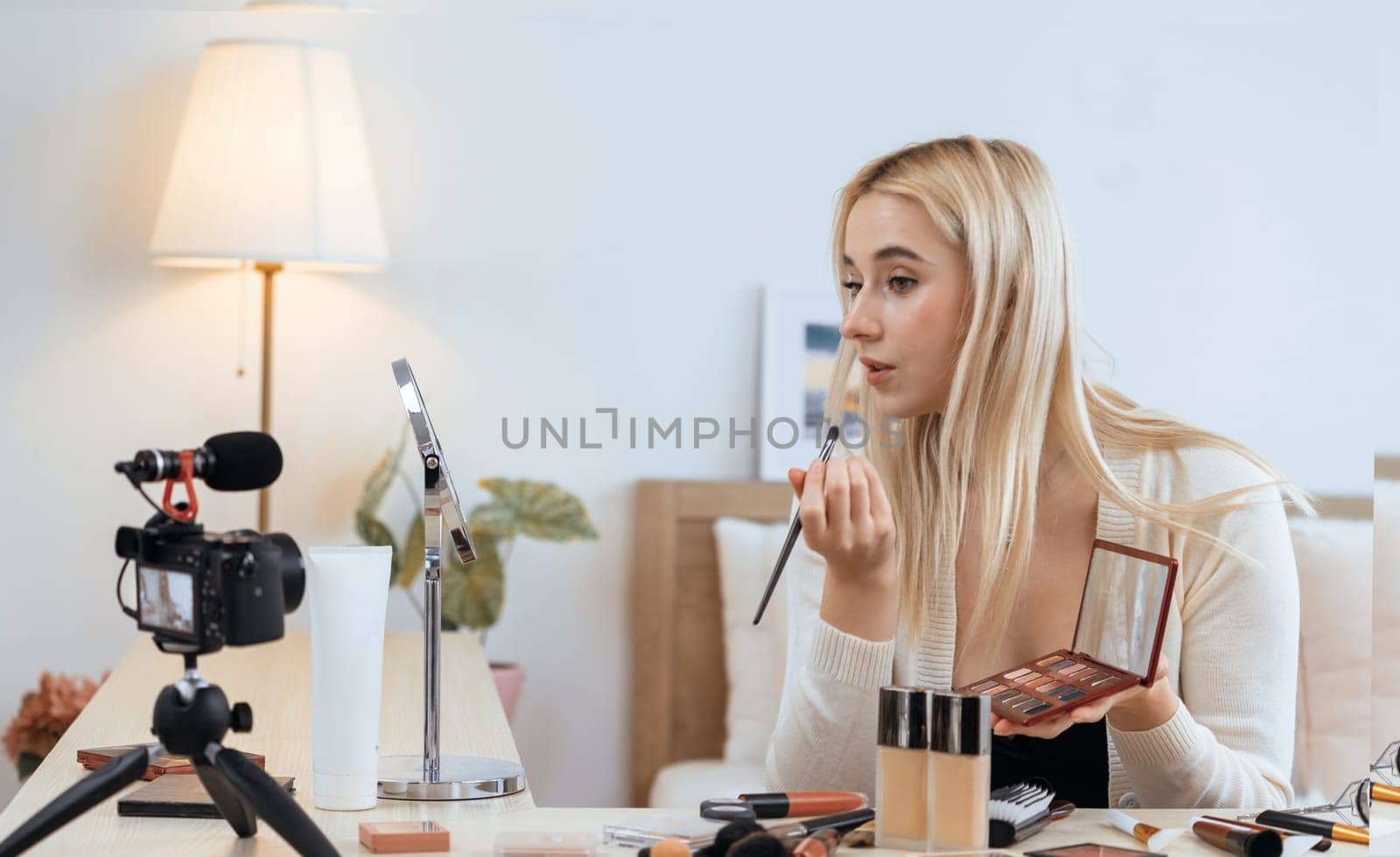 Young woman making beauty and cosmetic tutorial video content for social media. Beauty blogger smiles to camera while showing how to beauty care to audience or followers. Blithe