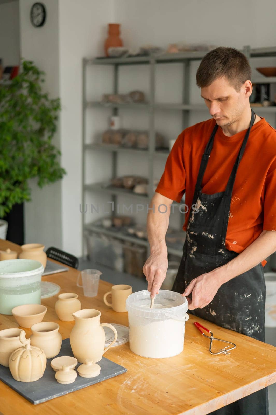 A potter applies glaze to a ceramic pot with a brush. Vertical photo