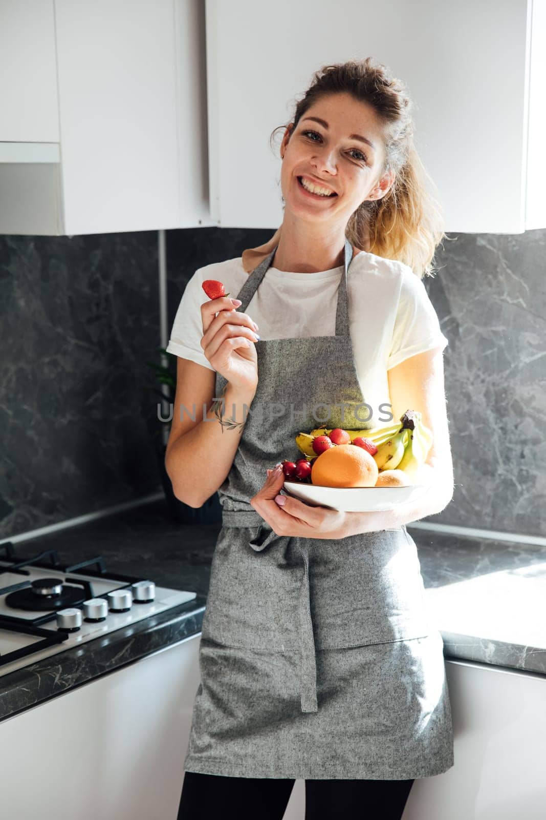 woman in an apron stands in the kitchen with fruits healthy food vitamins