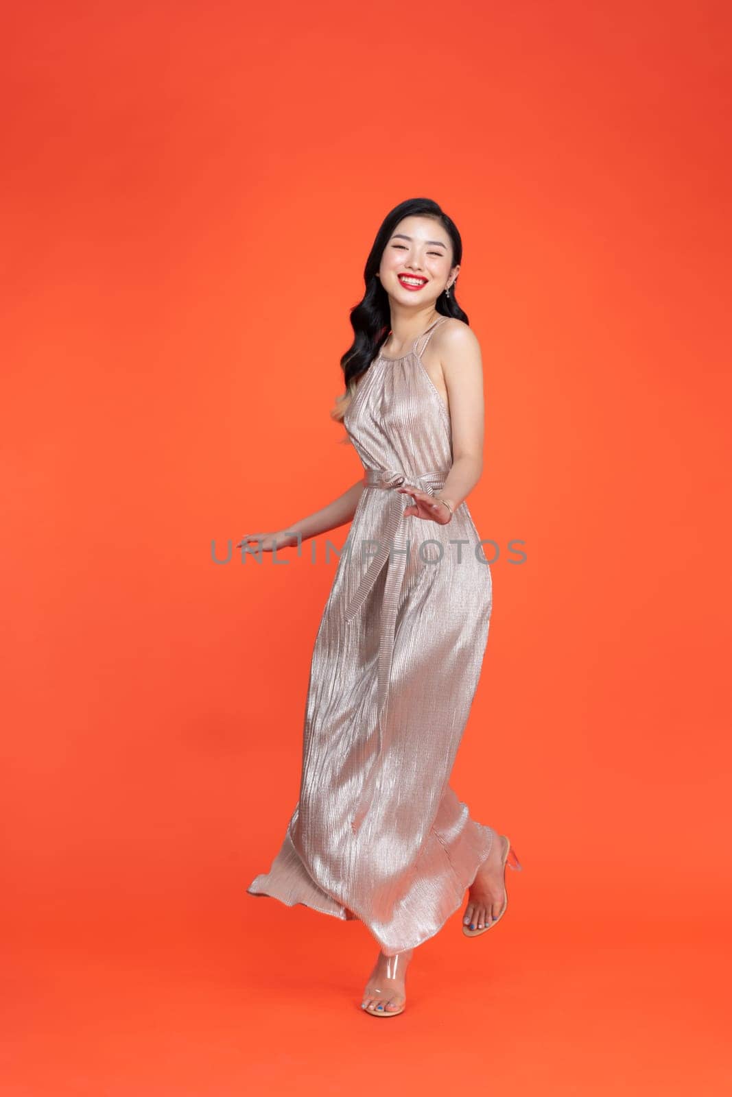 Portrait of a joyful beautiful woman in shiny dress having a party isolated over red background