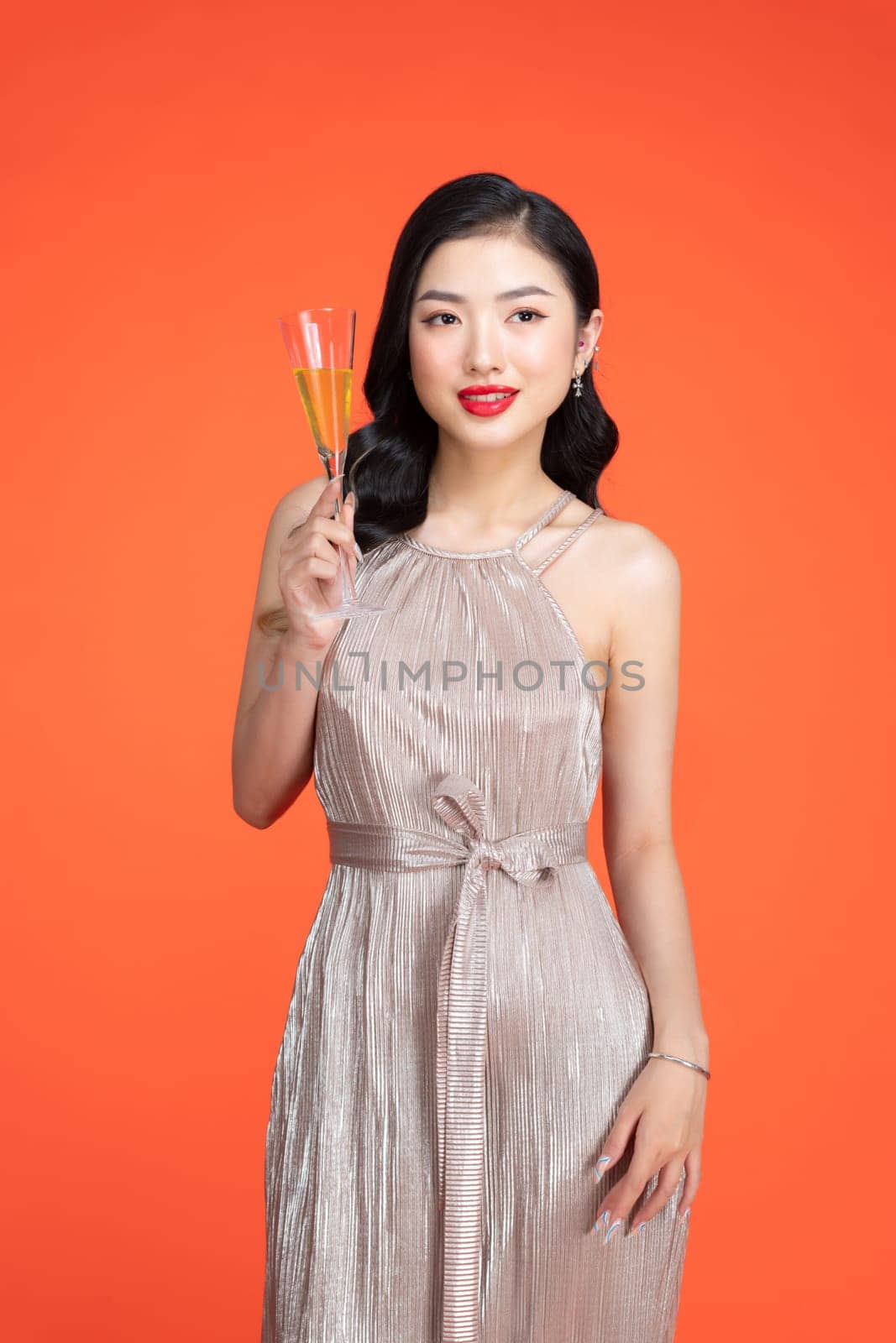 Fashionable lady in shiny stylish dress holding glass with drink on red background by makidotvn