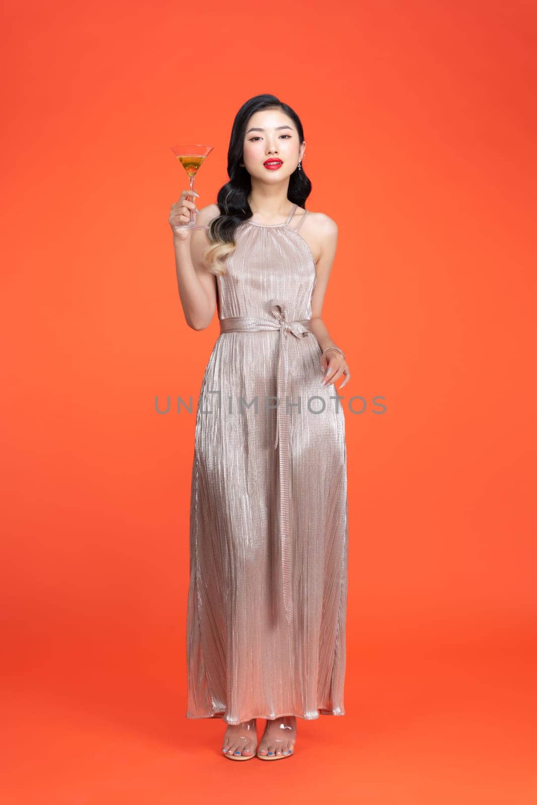 Fashionable lady in shiny stylish dress holding glass with drink on red background