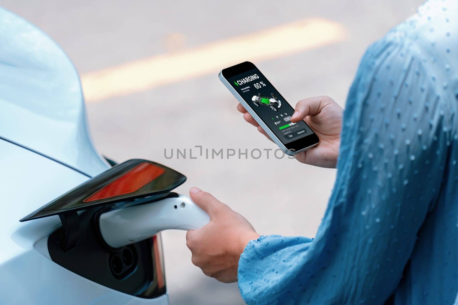 Hand insert EV charger plug into electric vehicle to recharge EV car, battery status display on smartphone EV application. Future alternative clean and sustainable energy for transportation. Perpetual