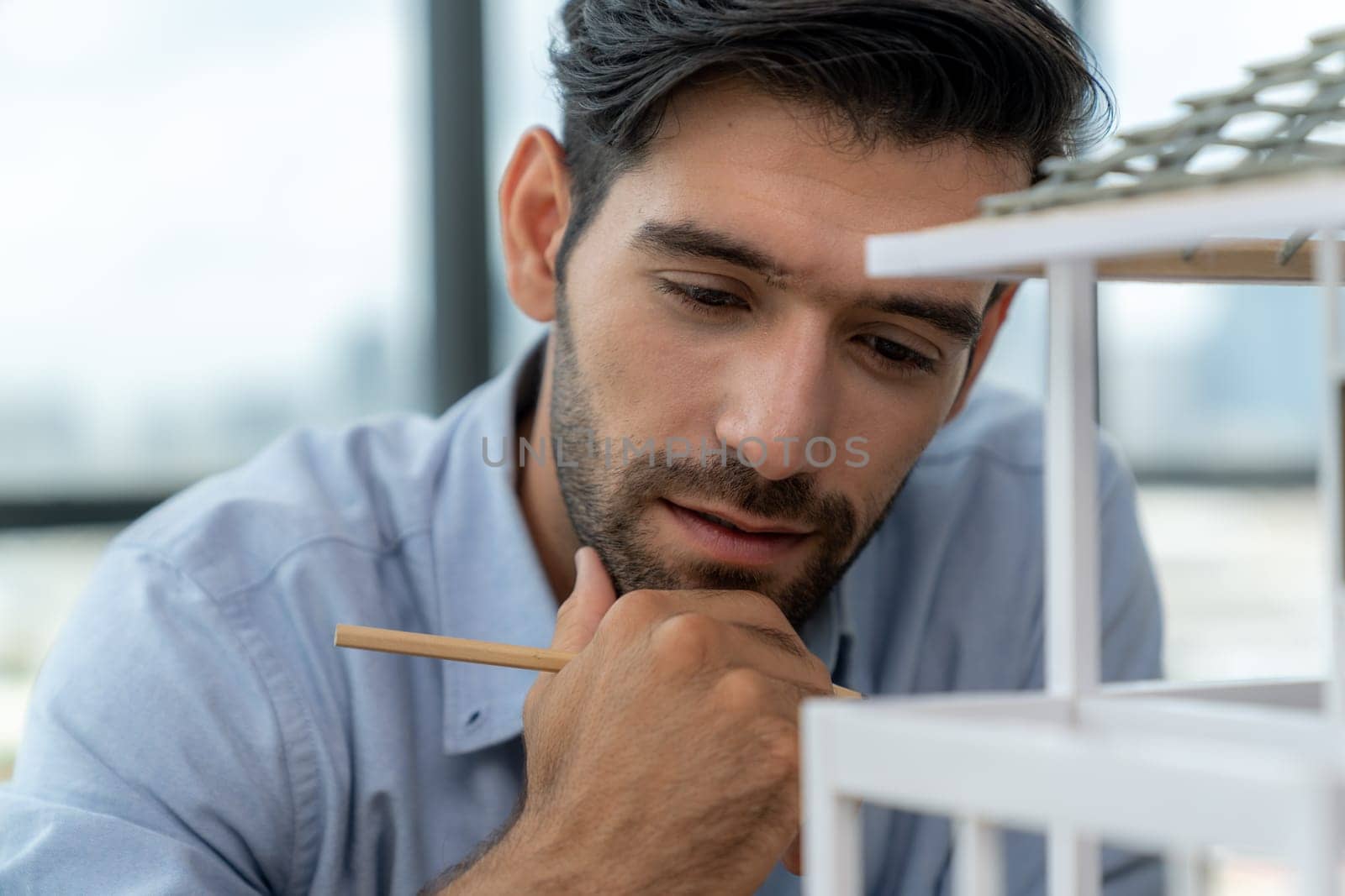 Closeup portrait of smart caucasian engineer face inspect house model while thinking about building construction at architect studio. Pointing pencil. Creative design, civil engineering. Tracery.