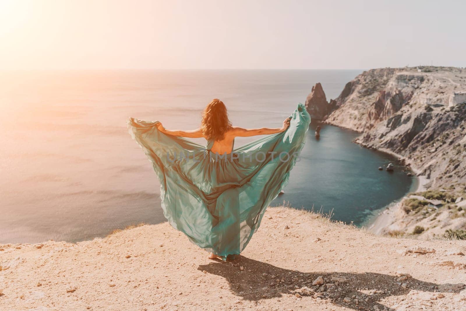 Woman green dress sea. Female dancer posing on a rocky outcrop high above the sea. Girl on the nature on blue sky background. Fashion photo