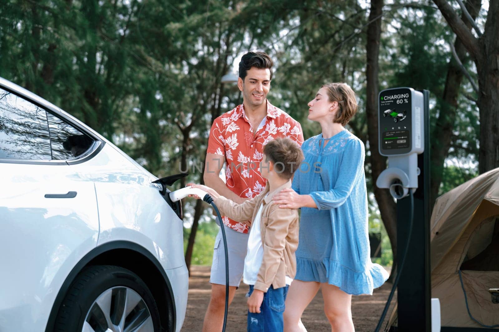 Outdoor adventure and family vacation camping in nature travel by eco friendly car for sustainable future. Lovely family recharge EV car with EV charging station in campsite. Perpetual