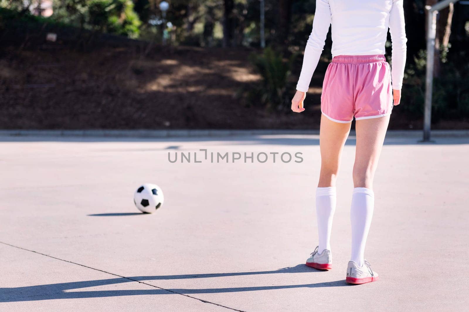 rear view of the legs of an unrecognizable young female football player preparing to kick a soccer ball on an urban field, concept of sport and active lifestyle