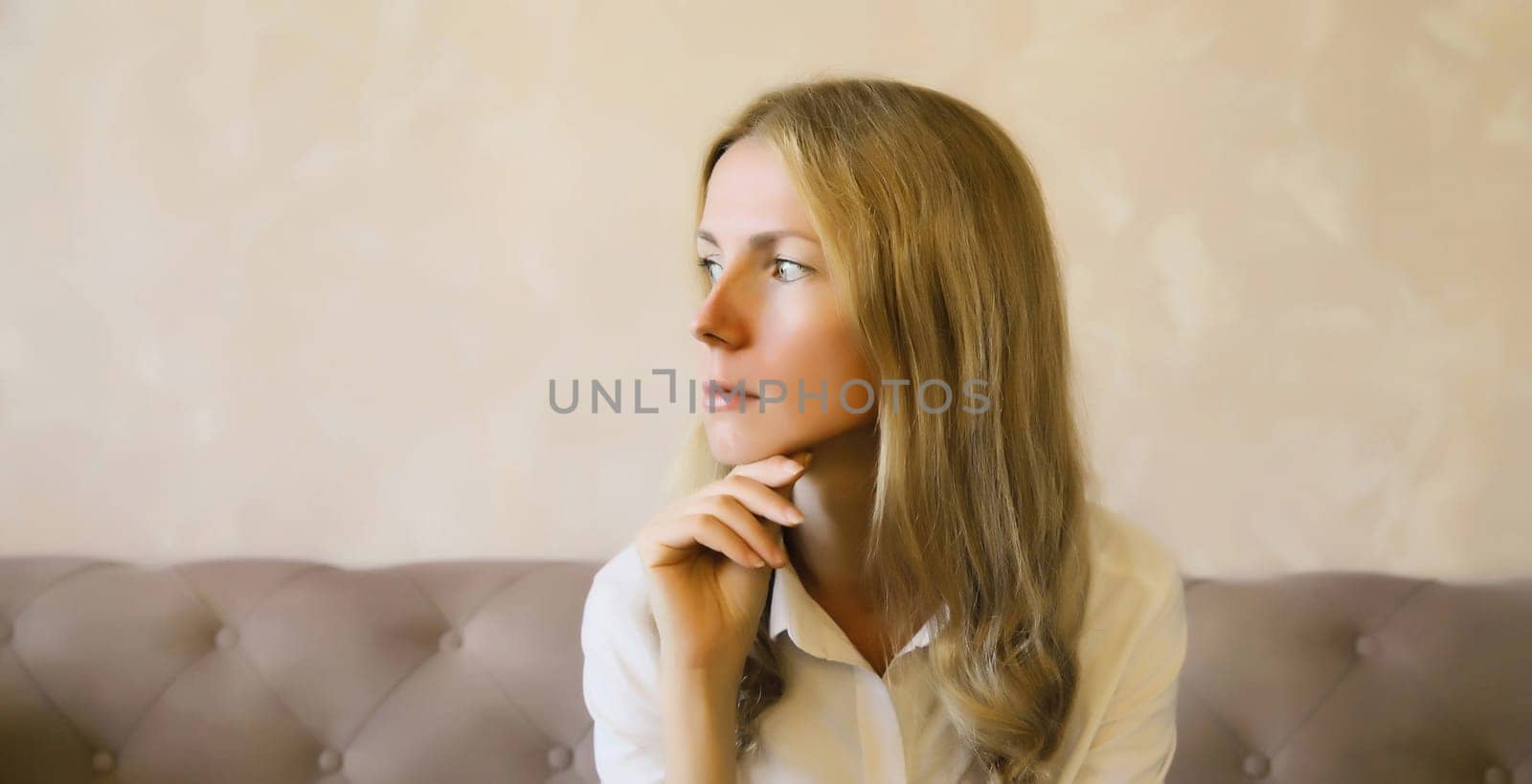 Pensive young woman thinks looks out the window, thoughtful girl suffering from depression sitting on the couch in living room at home