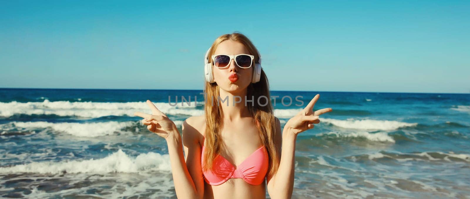 Summer vacation of happy young woman relaxing listening to music with headphones, modern girl having fun posing on the beach at sea coast on a sunny day