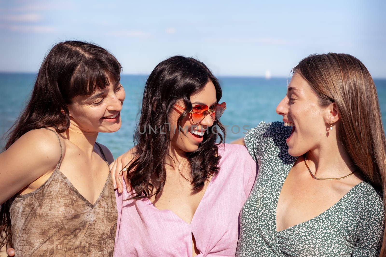 Cheerful multiethnic friends with sunglasses happy on vacation on the beach, looking at the camera.