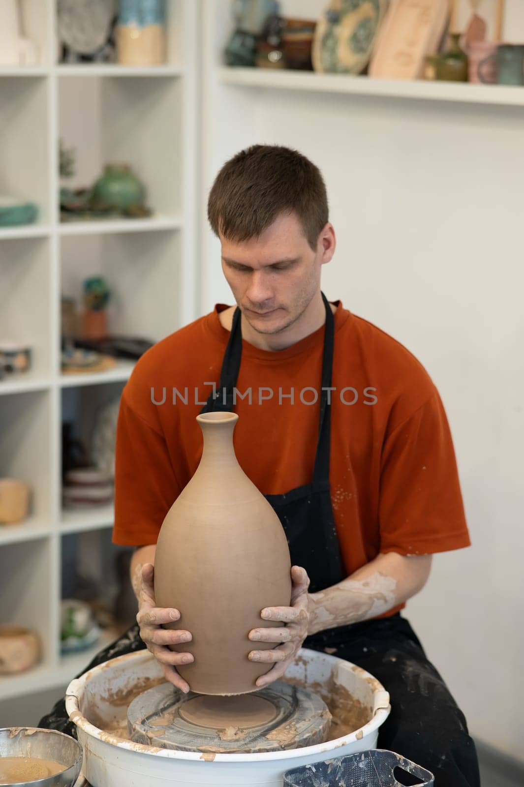 A man makes a ceramic vase on a pottery wheel. Vertical photo