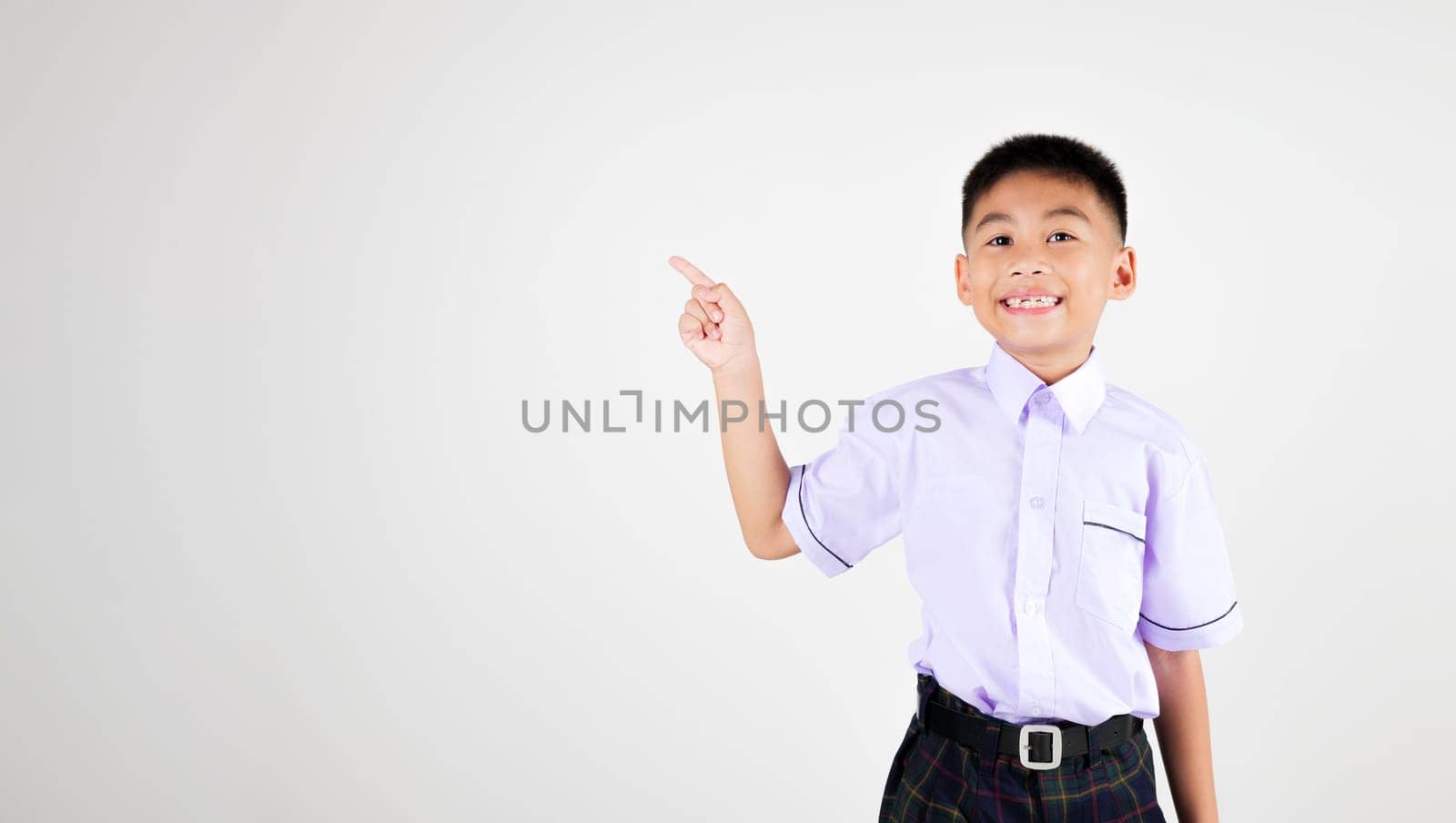 Portrait smile Asian little boy primary posing point finger to side away studio isolated white background, happy cute man kid wear school uniform plaid innocence and curiosity by Sorapop