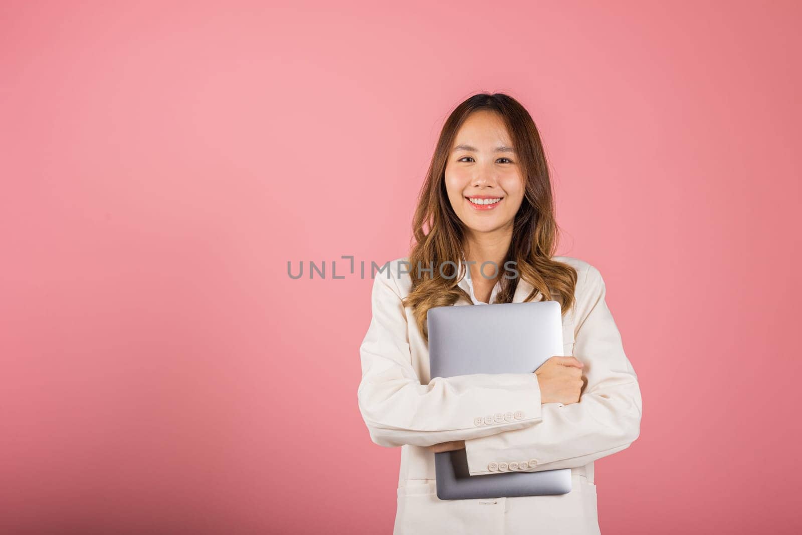 Front view woman smiling confident smiling holding closed laptop, Portrait excited happy Asian young female person hugging close cover computer device studio shot isolated on pink background