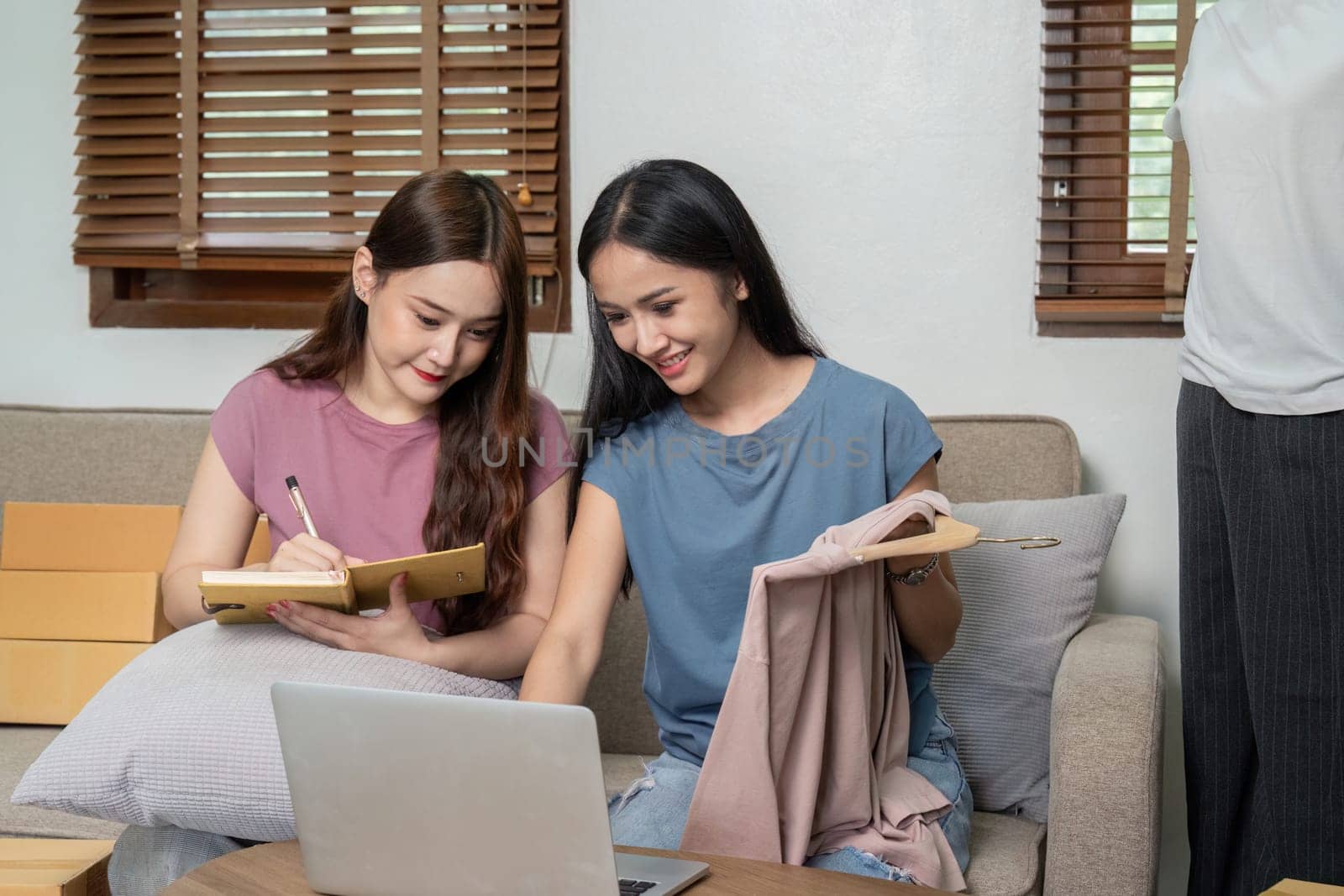 Lesbian couple working together on their online clothing business, using a laptop and taking notes in a cozy home setting.