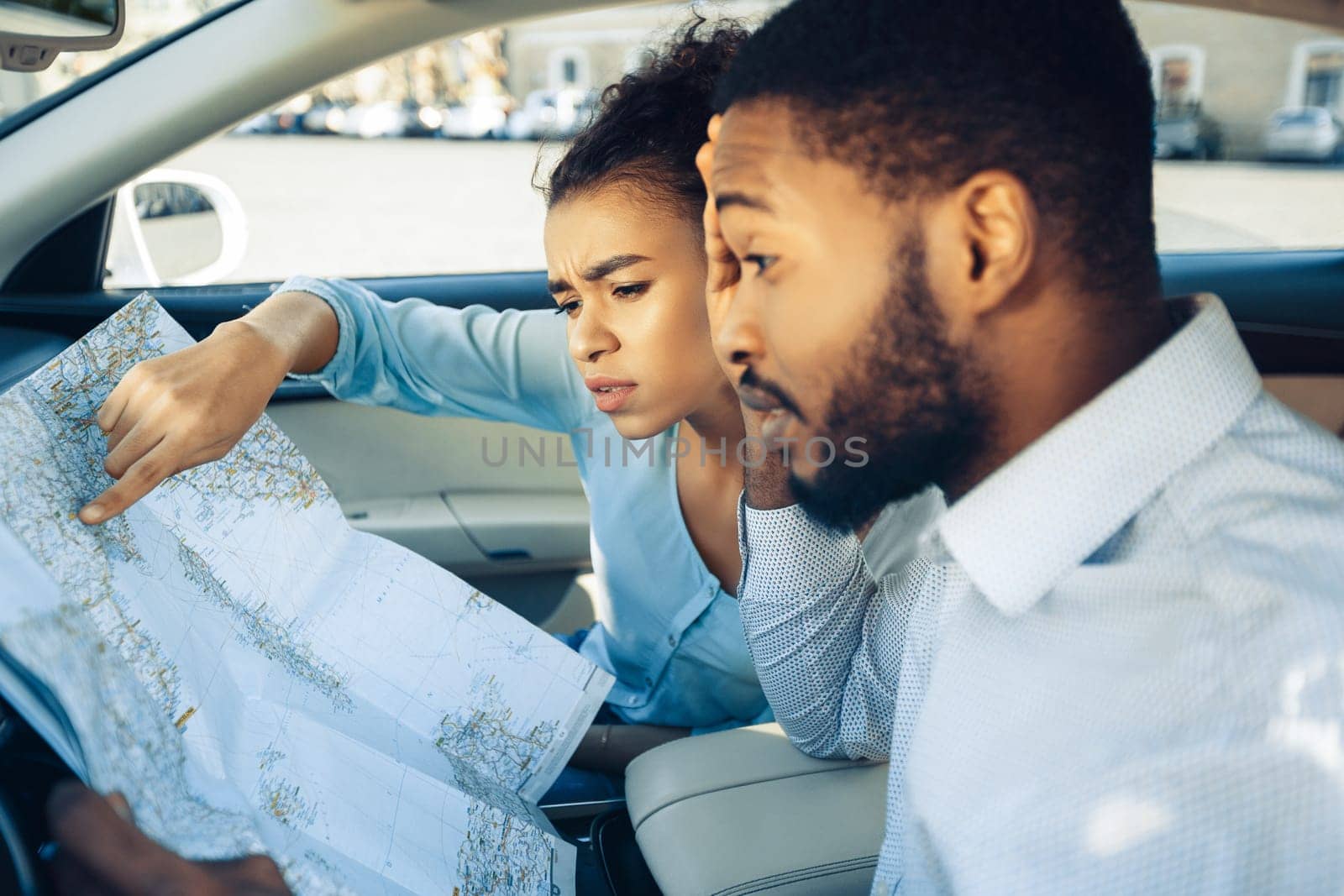 African American young couple is looking at a map in a car. They are both dressed casually. The woman is pointing at the map, and the man is looking at it intently.