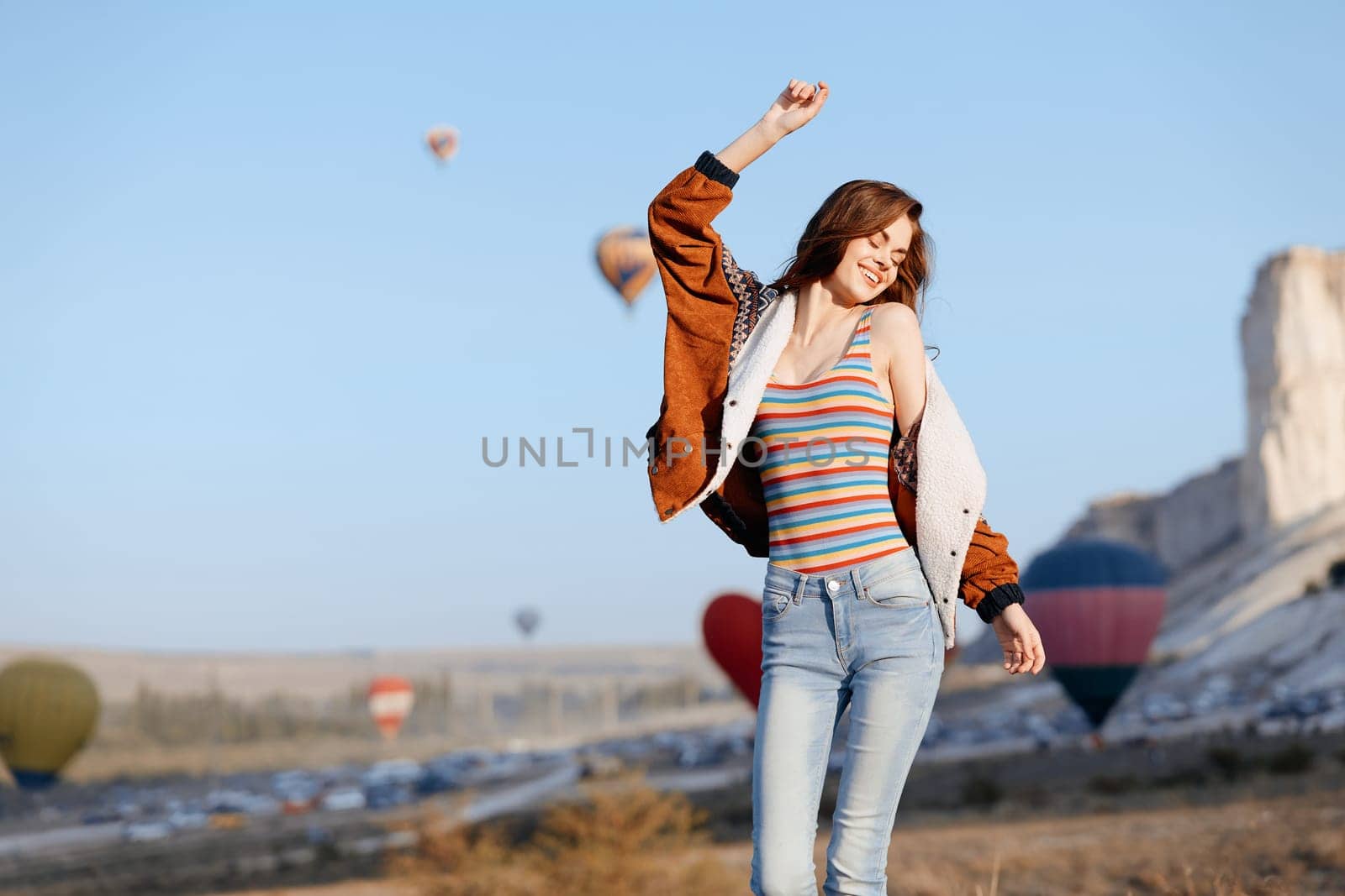 joyful woman leaping with striped shirt as colorful hot air balloons float in the sky
