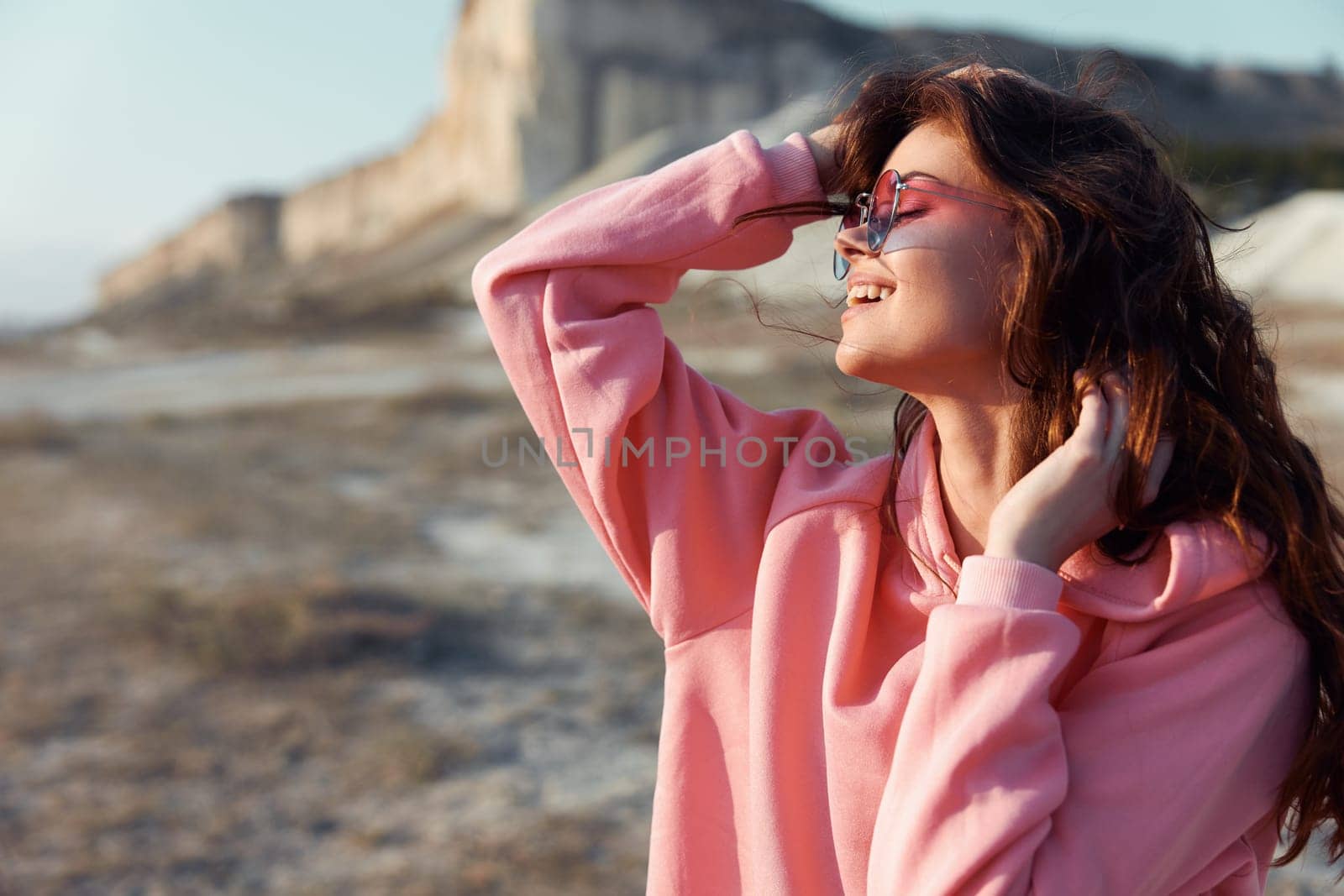 Serene woman in pink sweatshirt and sunglasses standing on beach with majestic mountain backdrop by Vichizh