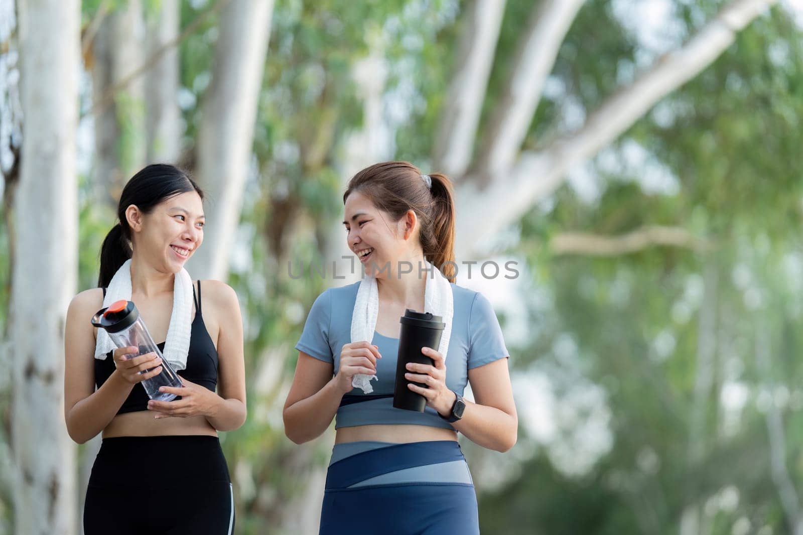 Two friends share a joyful moment while running in the morning, staying hydrated and enjoying the fresh air in a beautiful outdoor environment.