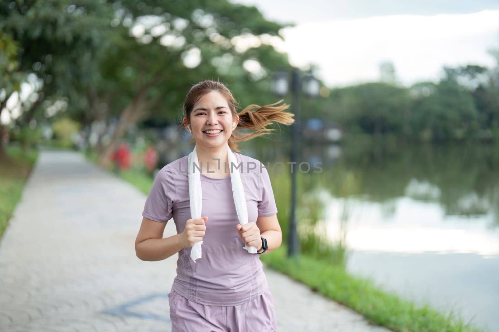 Young Woman Enjoying a Morning Run by the Lake in a Park with a Smile on Her Face by nateemee