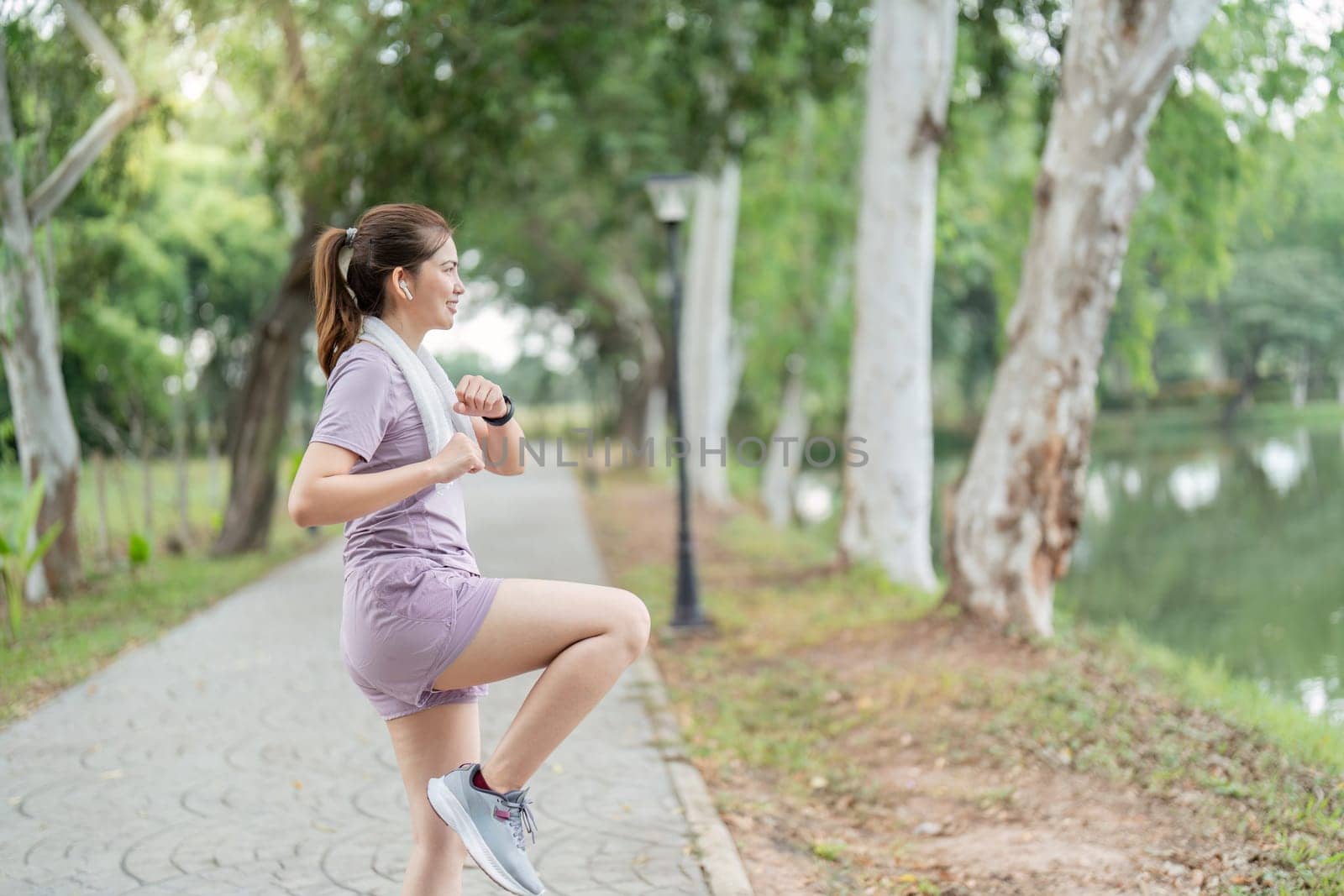 Morning Exercise Routine. Woman Running and Stretching in Park with Trees and Lake in Background by nateemee