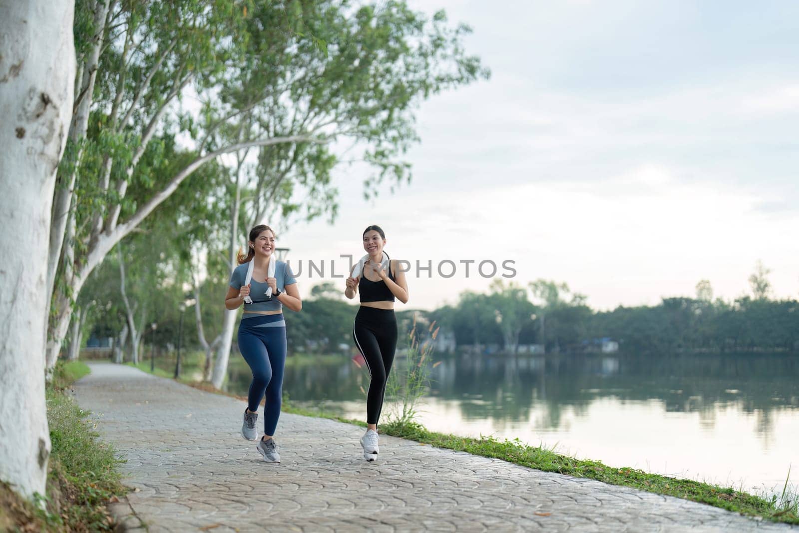 Two Friends Running Together in the Morning by a Scenic Lakeside Path for Exercise and Fitness by nateemee