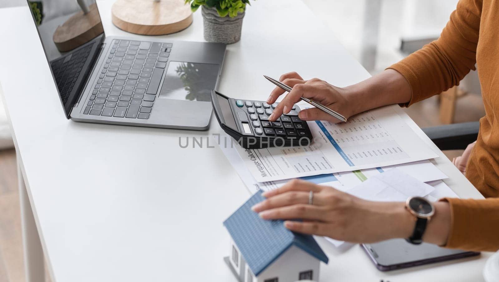 Woman Calculating Real Estate Transaction with Calculator and Documents at Modern Office Desk by wichayada