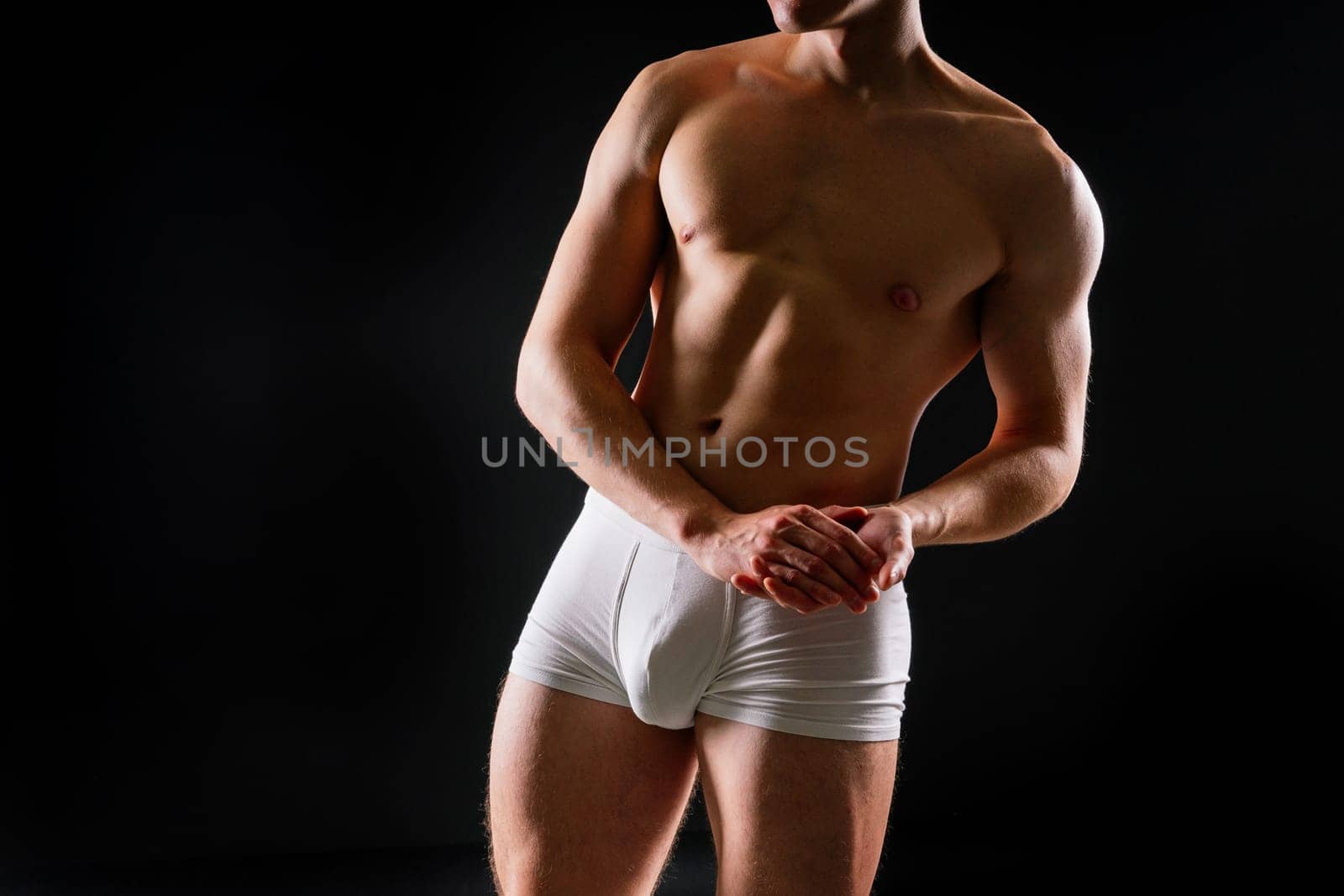 Man holds barbell weights, young adult strong male in a white briefs, studio shot. Sport and muscles.