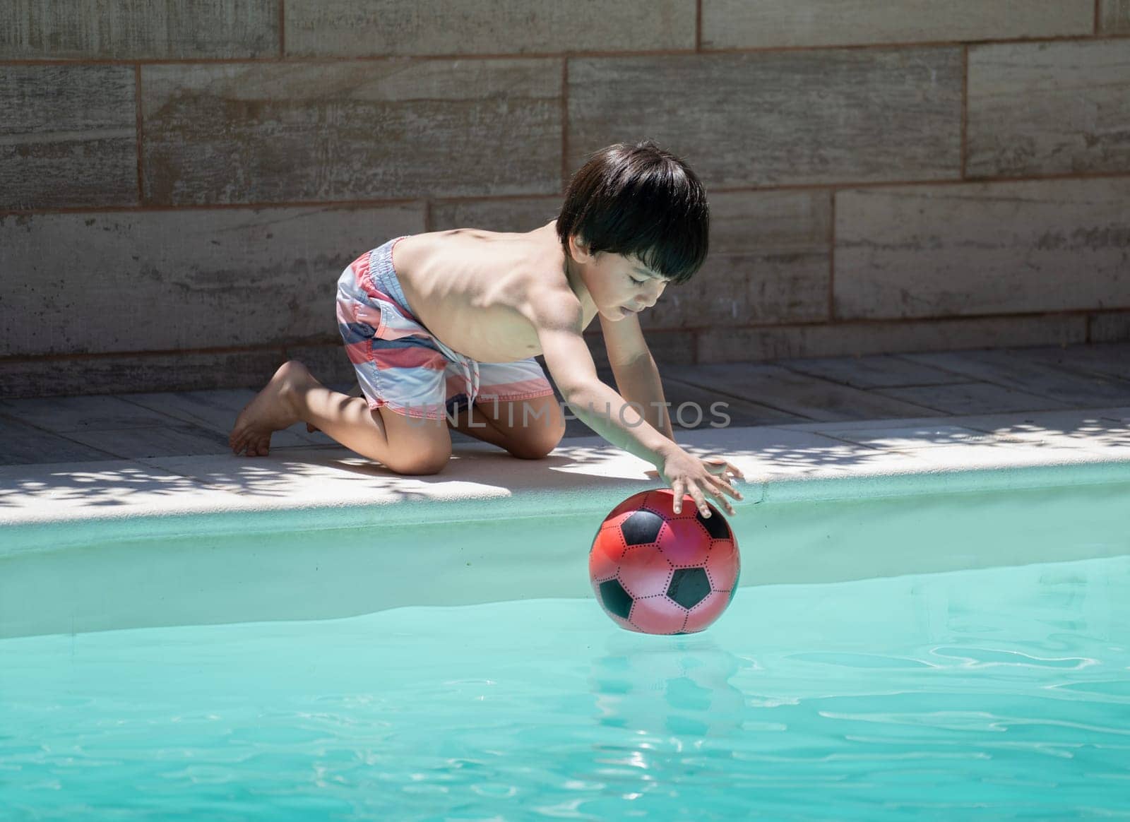 Dominican young boy playing in the pool on holidays trying to catch up his red ball.