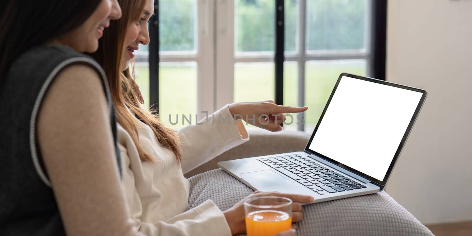 Lesbian Couple Relaxing at Home with Mock Up Laptop Screen, Pointing and Smiling, Cozy Living Room Setting by nateemee