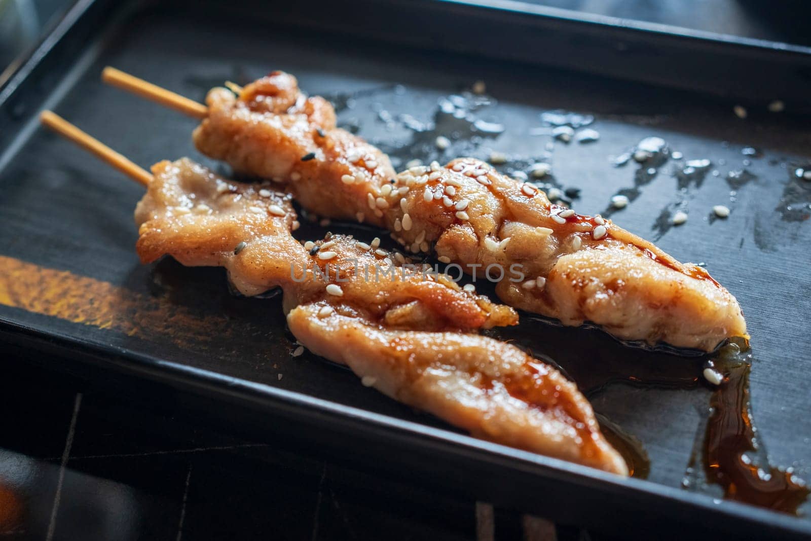 Nice view of Teriyaki chicken skewers on black plate and soy sauce