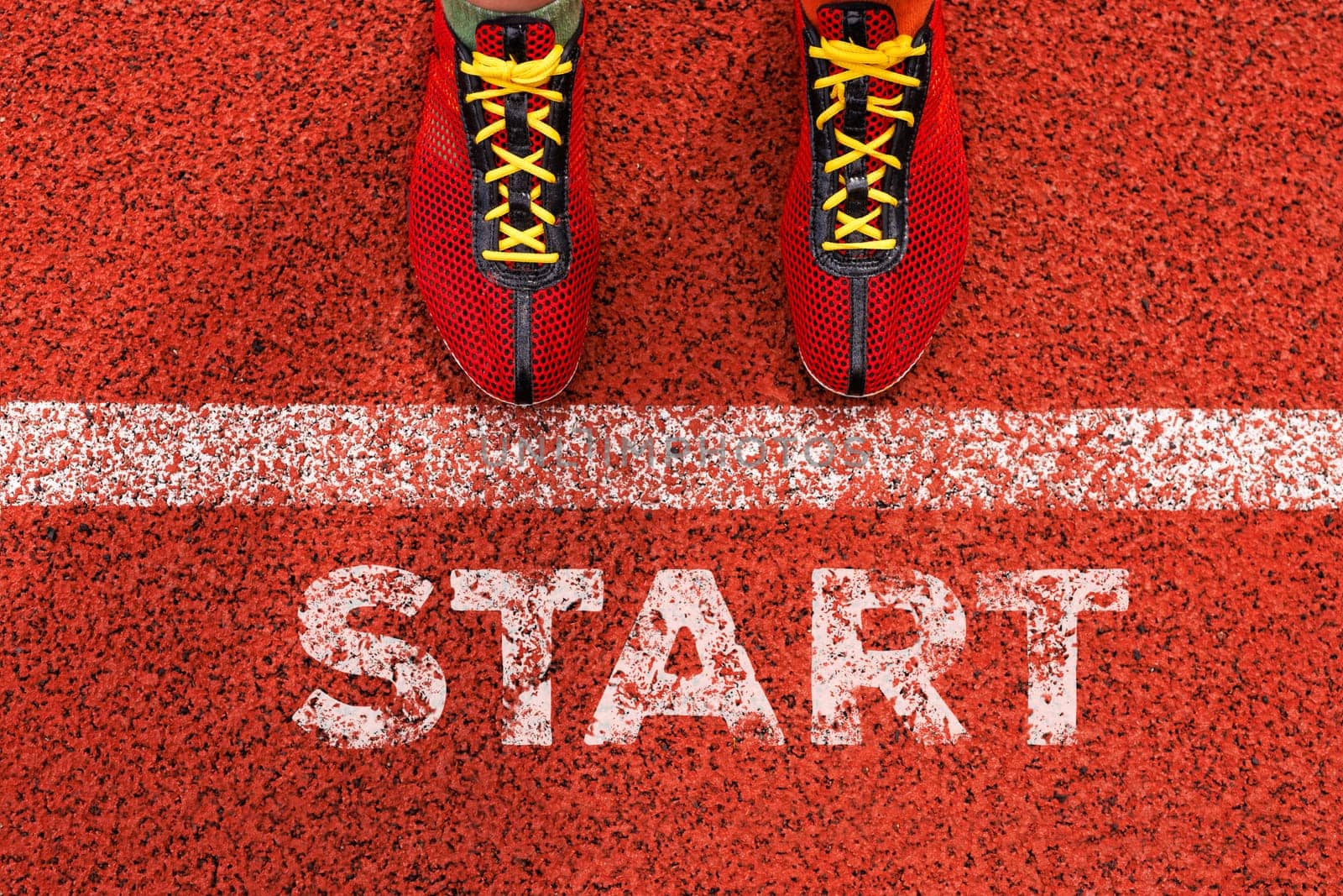 An athlete in red shoes is getting ready to start a race on a red track, showing determination and focus