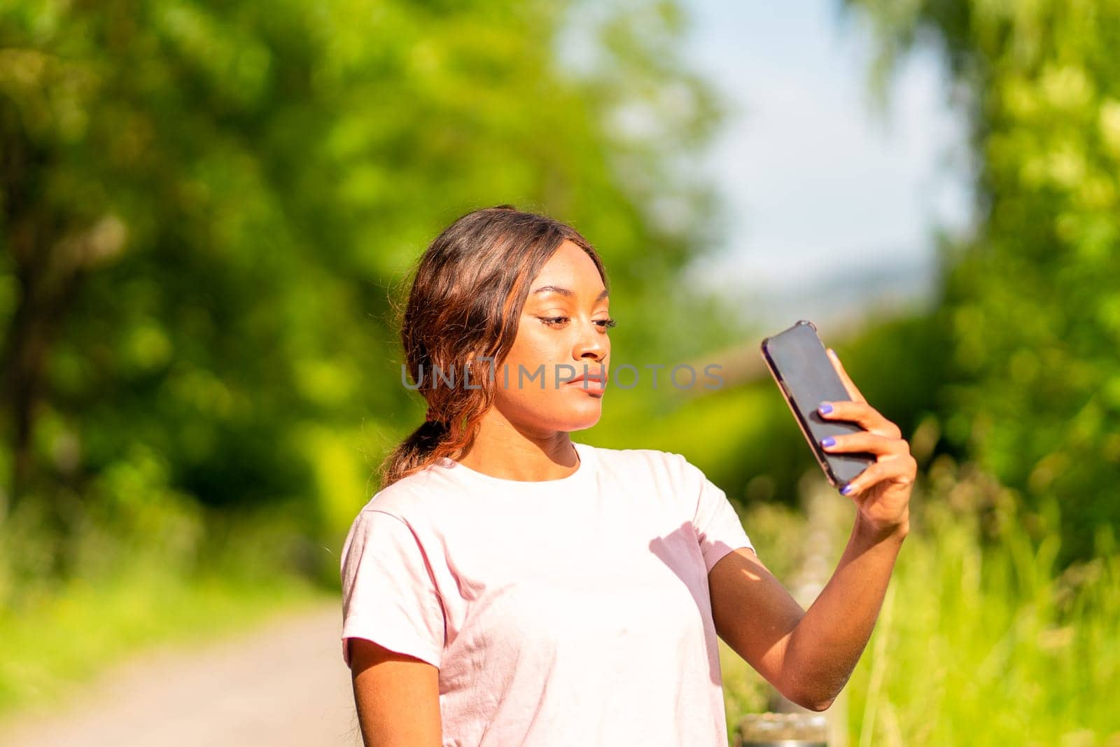 Young black woman with her phone taking selfie in a park on an October afternoon.