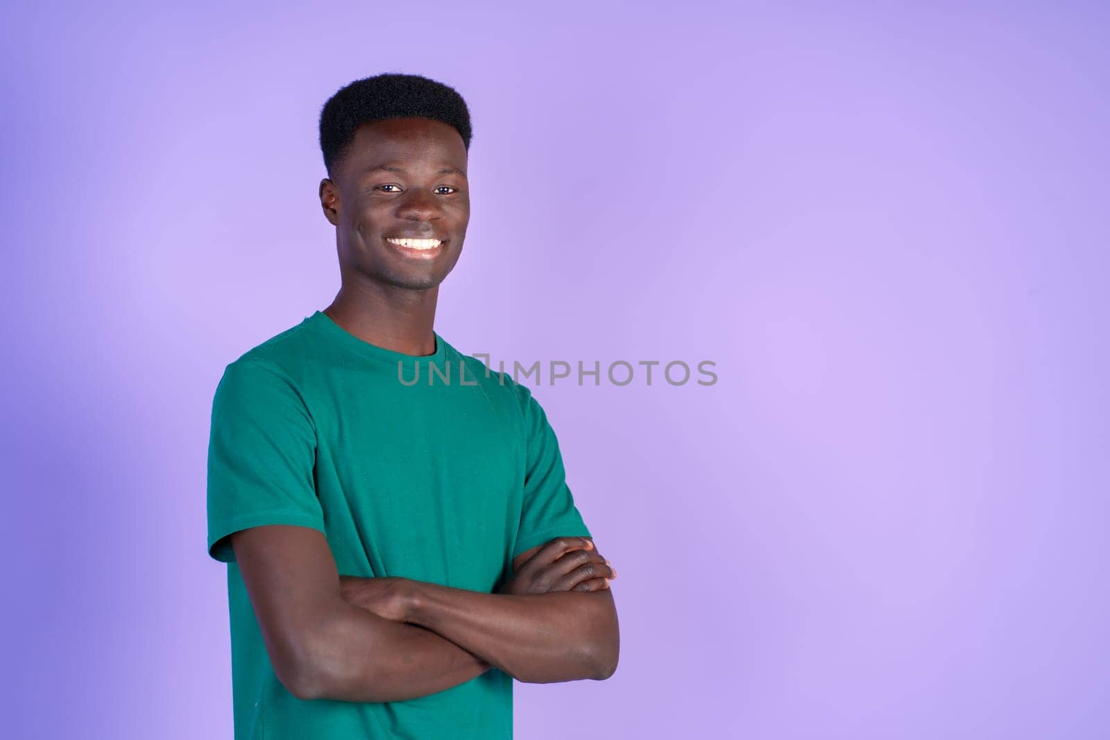 Young smiling black man wearing green t-shirt, arms crossed, isolated on a violet background. with copyspace. by Ceballos