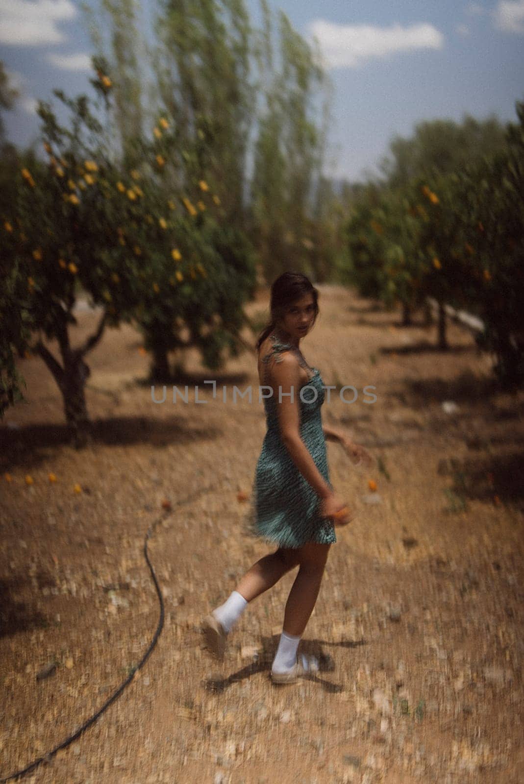 A young woman enjoys a leisurely stroll through a sunlit orchard, surrounded by nature and serenity