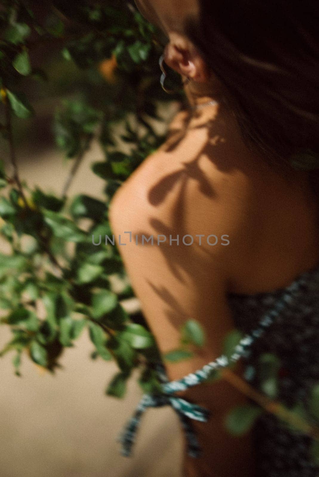 Artistic photo of a woman in leaves with soft focus and shadows in a sunny garden, creating an ethereal ambiance