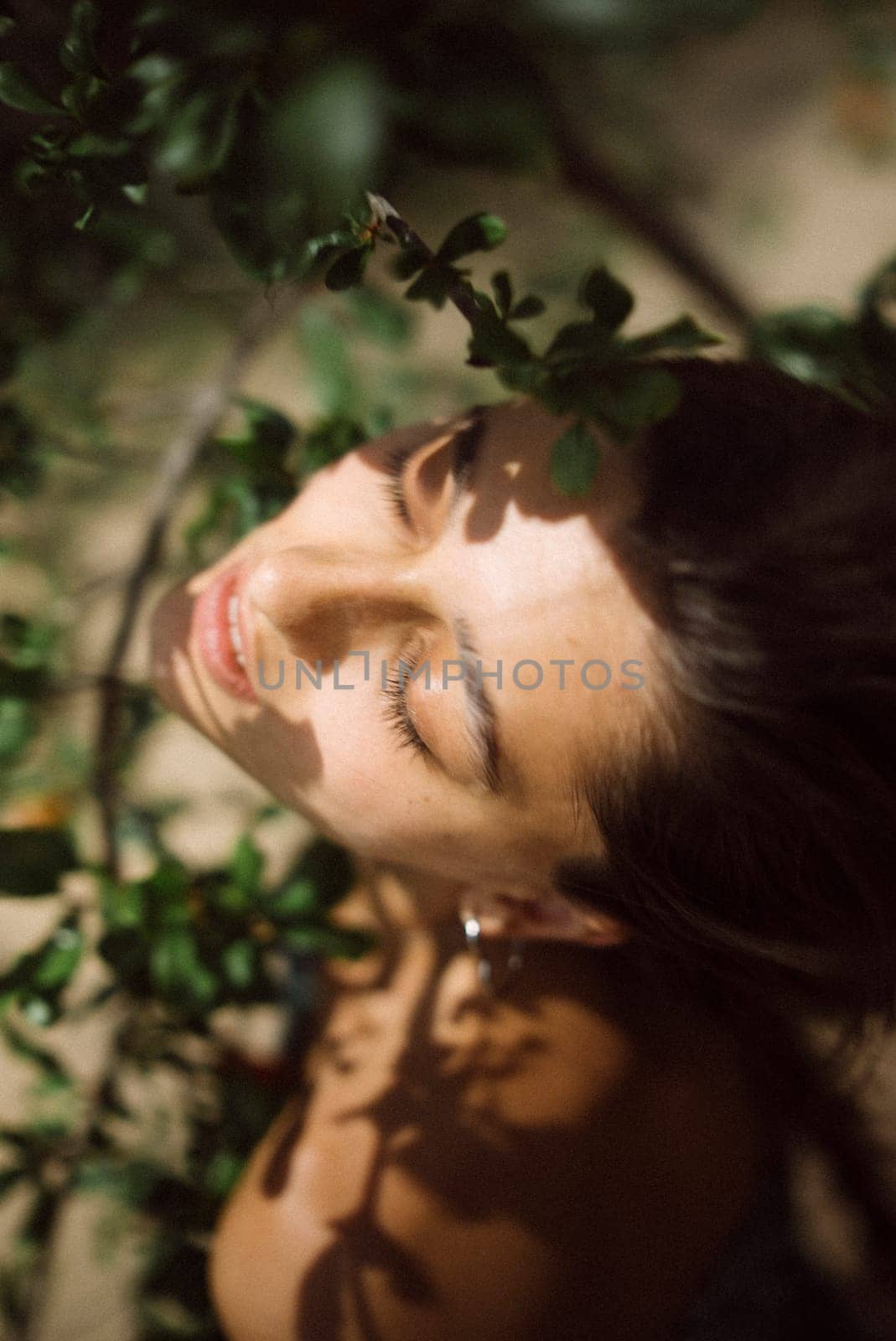 In the serene scene, a woman peacefully basks in the sun amidst vibrant green leaves, radiating beauty and tranquility