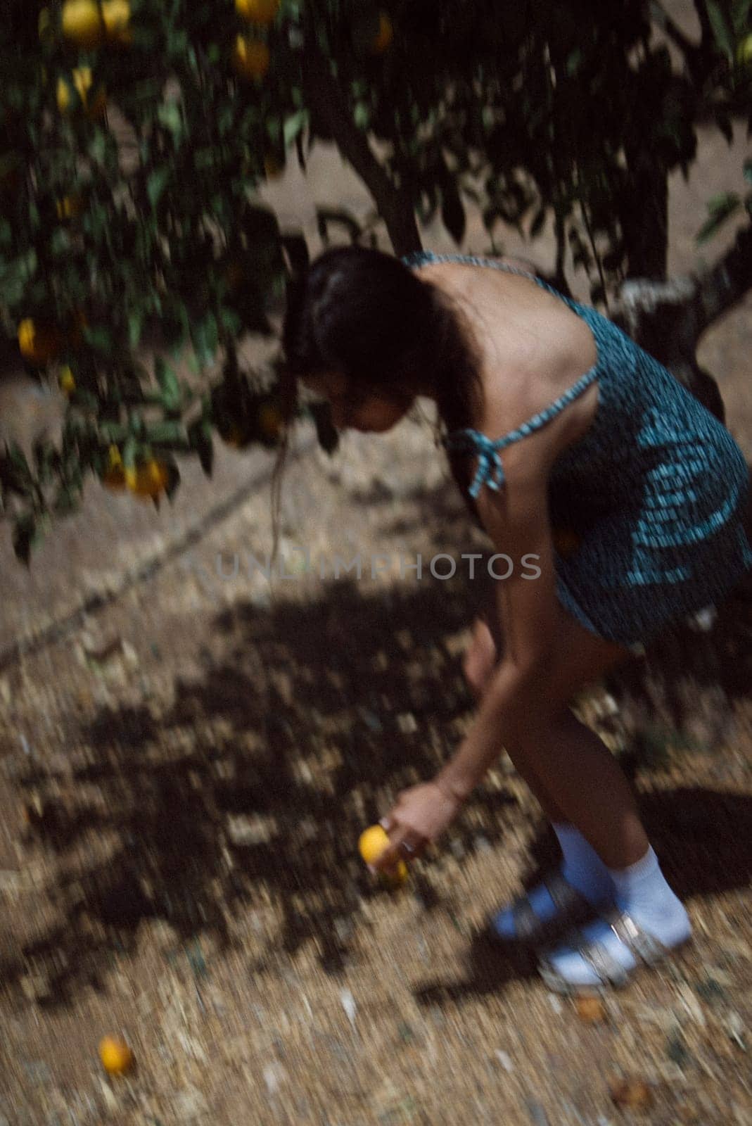A woman in a green dress and white shoes picking fruit in a sunny orchard, enjoying the outdoor activity