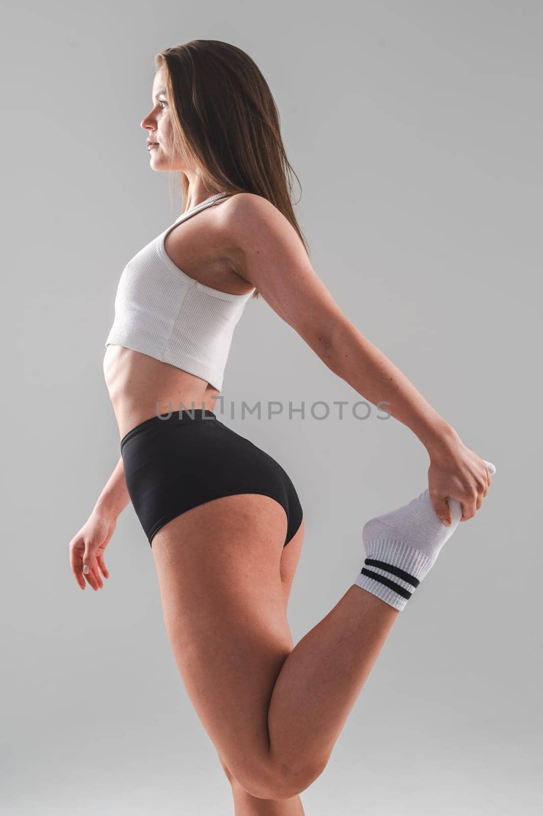 Athletic Caucasian woman stretching her quadriceps on a white background. Vertical photo. by mrwed54