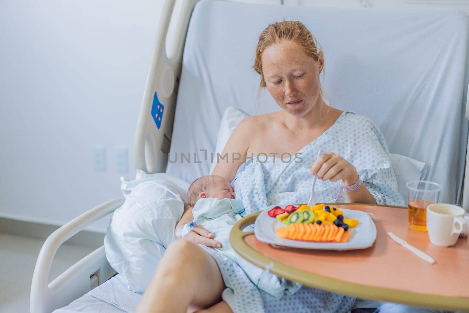A woman breastfeeds her baby in the hospital while simultaneously having lunch herself. This moment of multitasking illustrates the balance between motherhood and self-care, emphasizing maternal dedication and the nurturing atmosphere of the hospital ward.