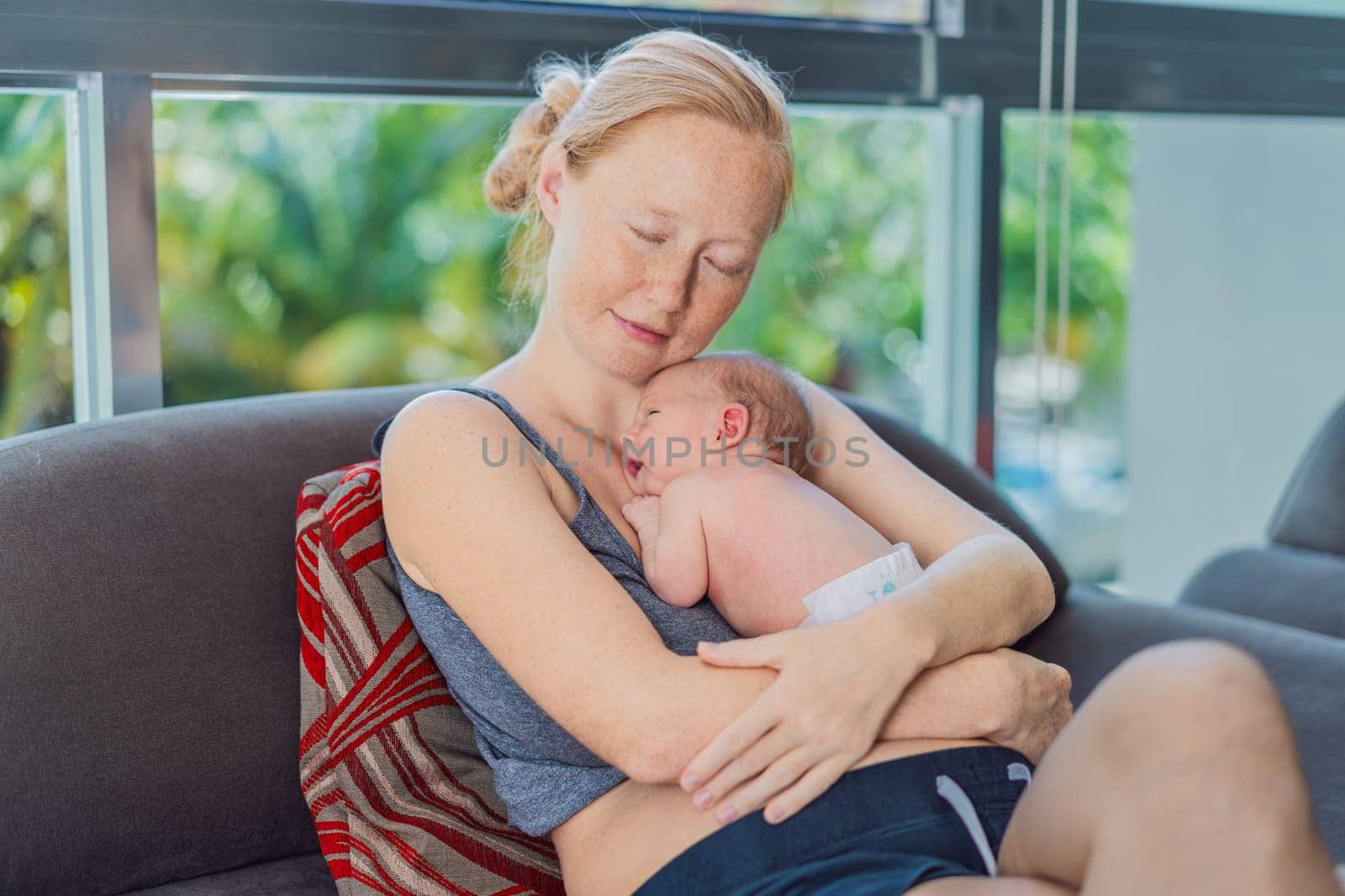 Mom with newborn baby relaxing on the sofa at home. This tender moment highlights the bond between mother and child in a comfortable and loving family environment.