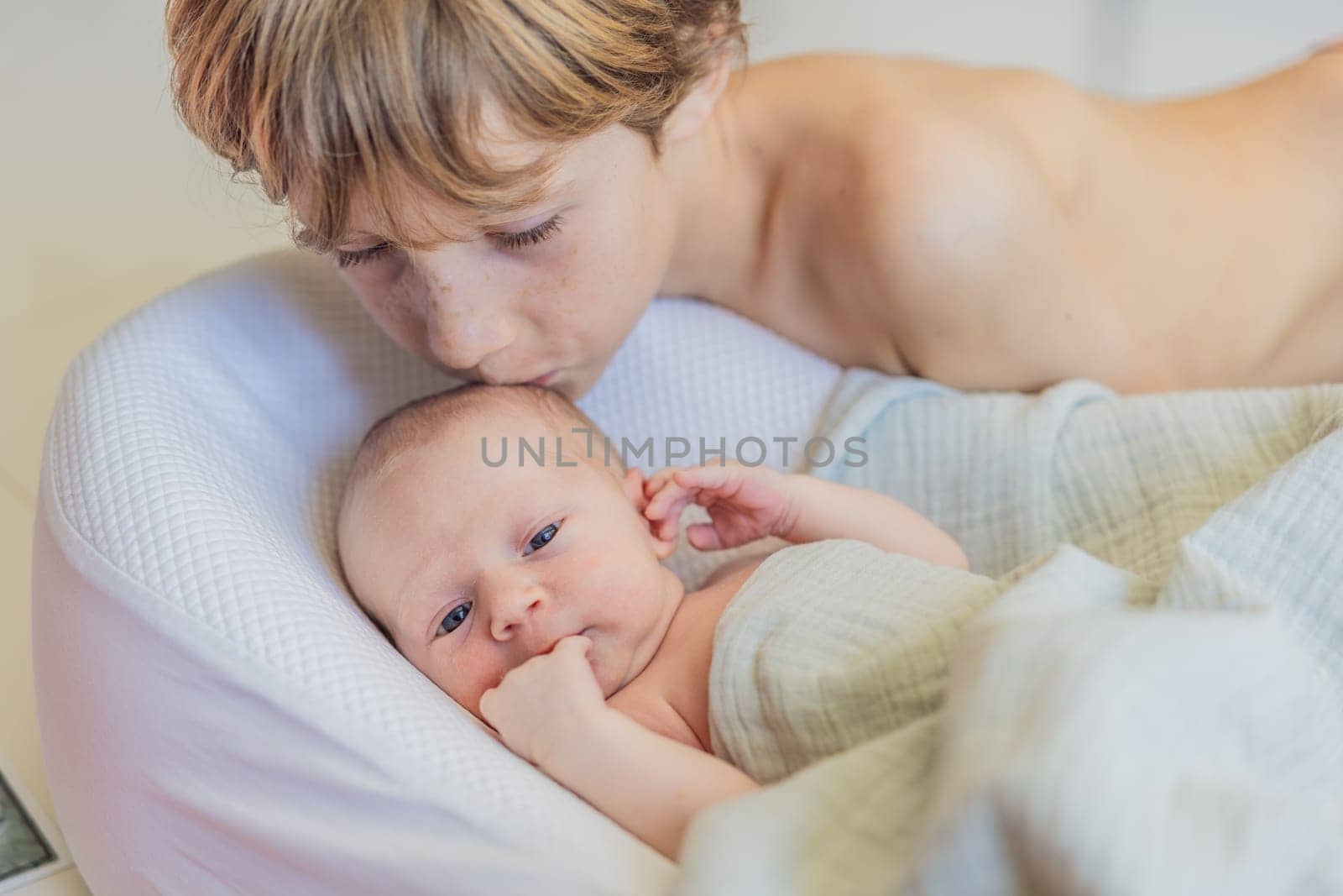 Older brother kisses newborn baby brother. This heartwarming moment captures the sibling bond and love, highlighting family connections and the tender care of an older sibling for the newest family member.