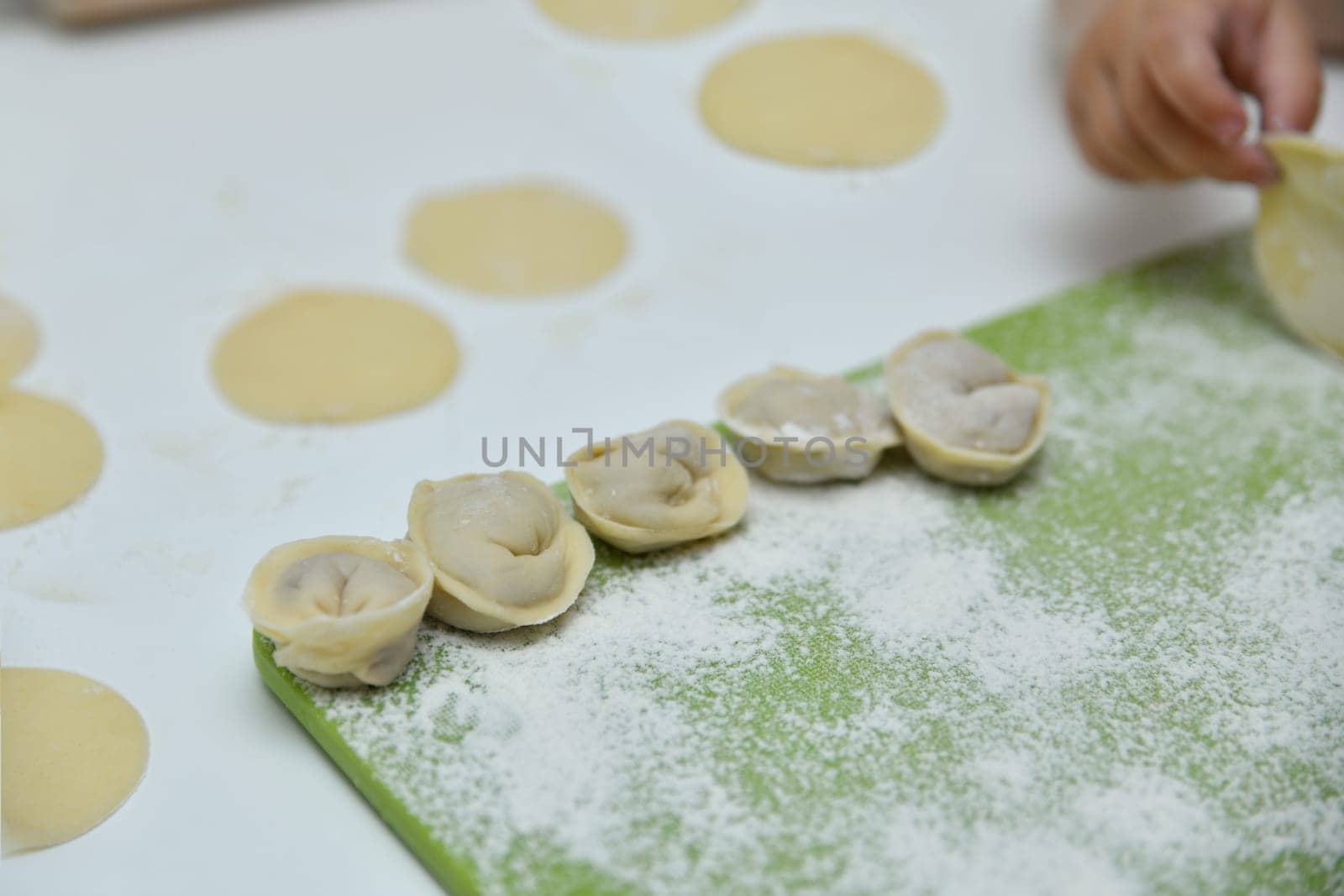 A child's hand making Russian dumplings in a kitchen