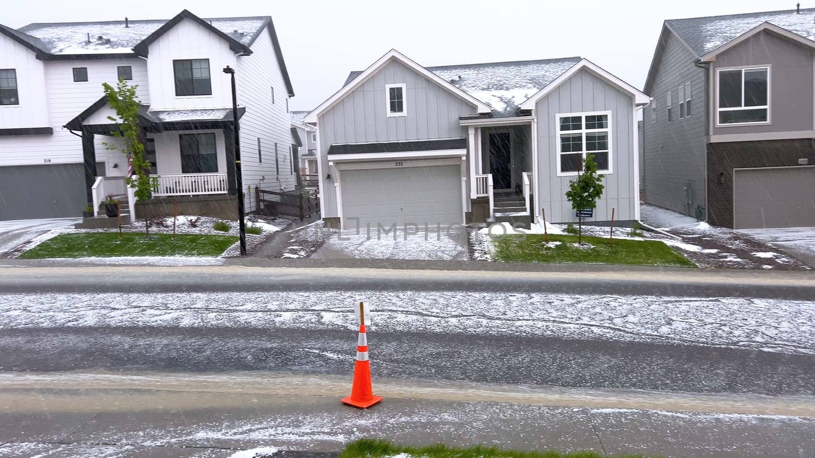 Castle Rock, Colorado, USA-June 12, 2024-Slow motion-A suburban neighborhood with modern houses covered in a layer of hail after a storm. The scene shows a driveway with a car parked, and the street littered with hailstones.