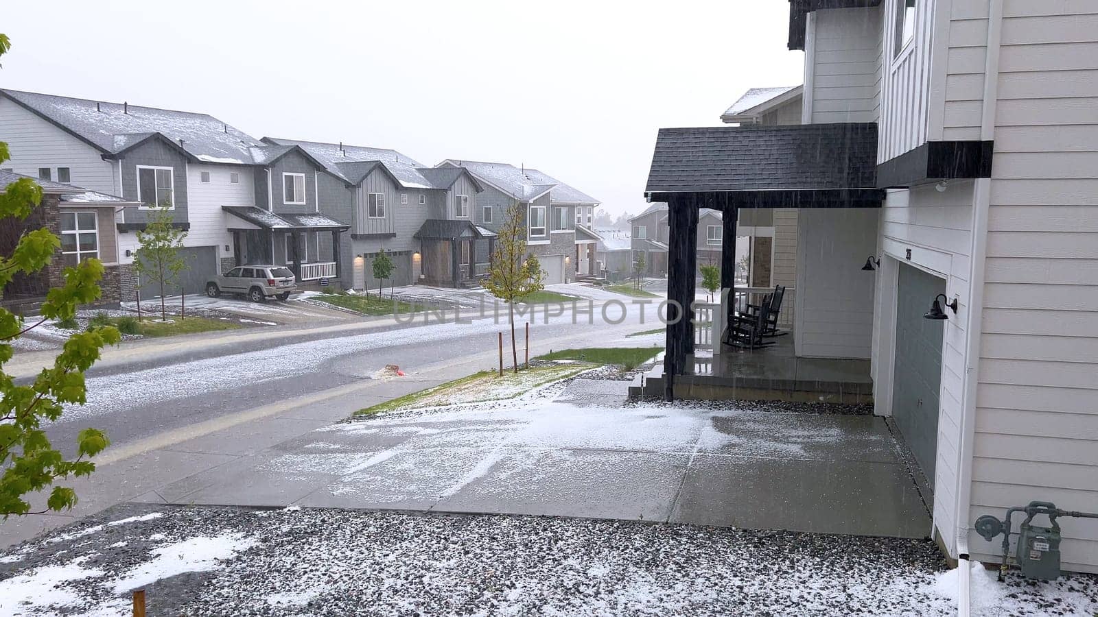 Castle Rock, Colorado, USA-June 12, 2024-Slow motion-A suburban neighborhood with modern houses covered in a layer of hail after a storm. The scene shows a driveway with a car parked, and the street littered with hailstones.