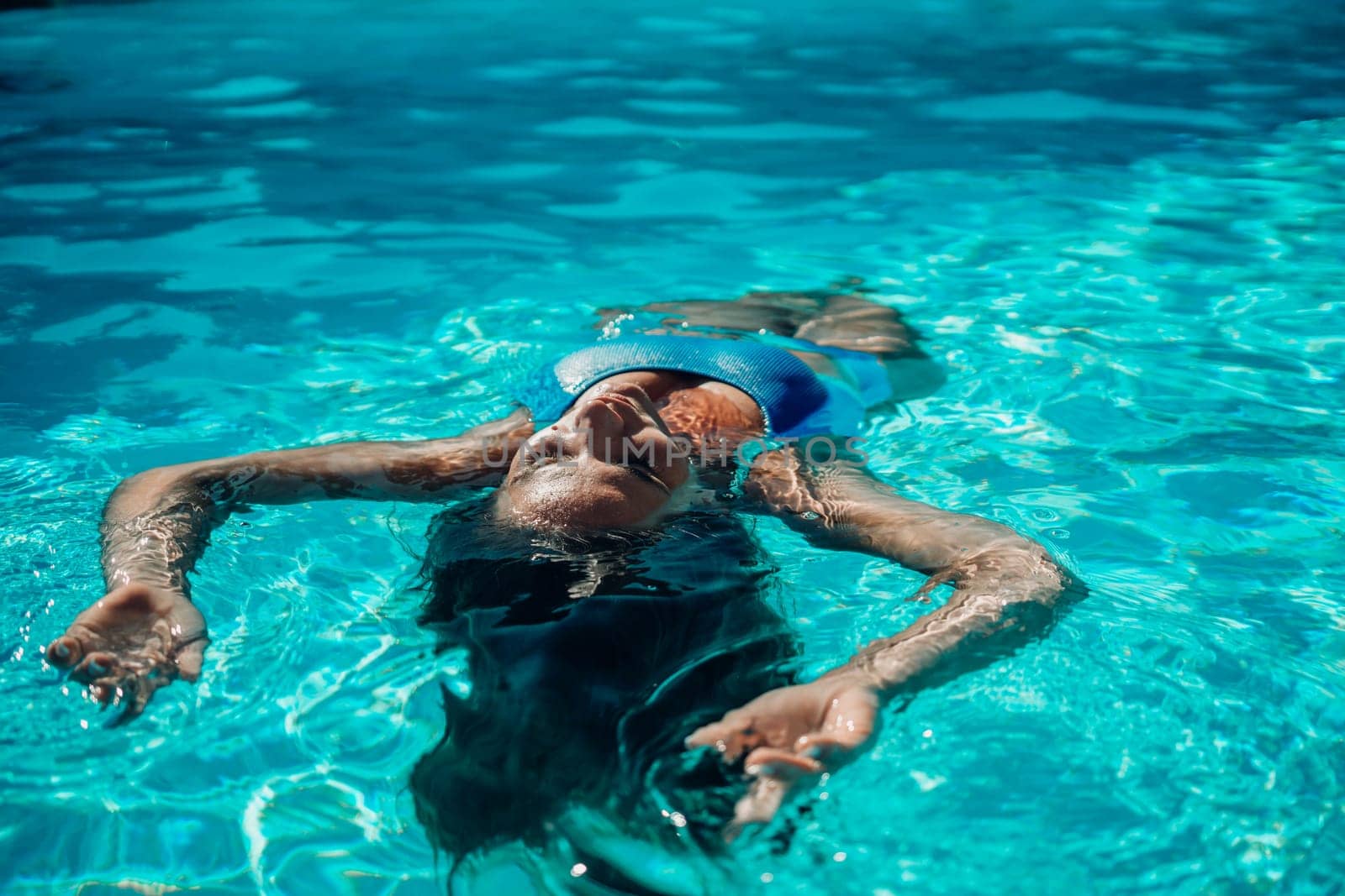 Woman relaxing swimming pool. Happy woman in a blue swimsuit floating in the pool, look form above by Matiunina