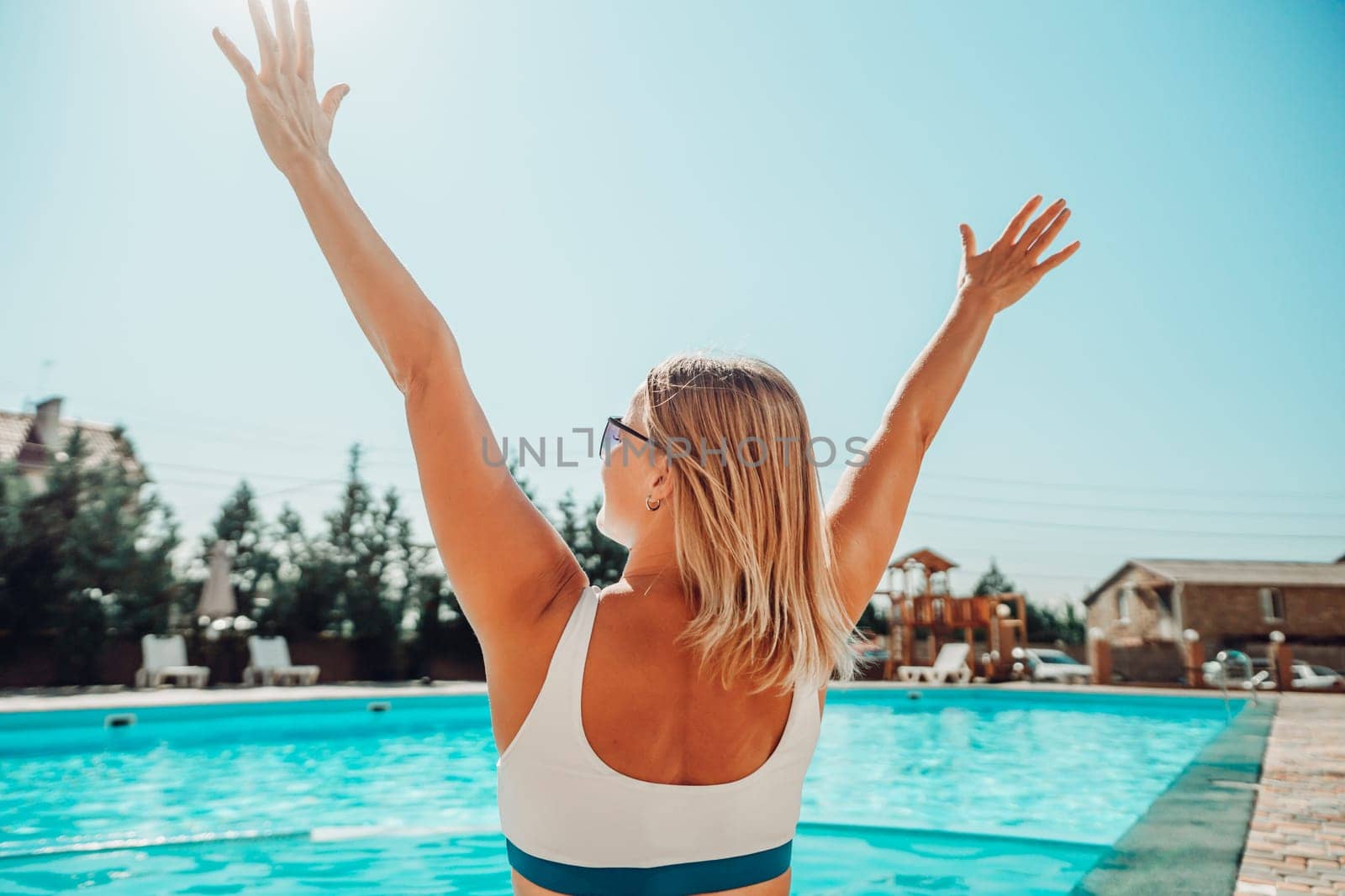 A woman is sitting in a pool with her arms raised in the air. Scene is joyful and carefree