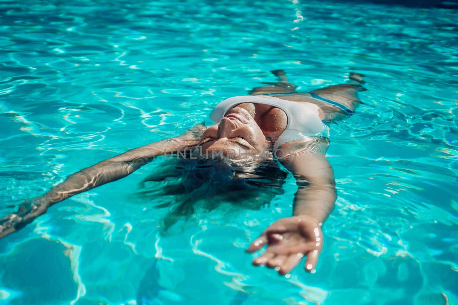 Woman relaxing swimming pool. Happy woman in a blue swimsuit floating in the pool, look form above.