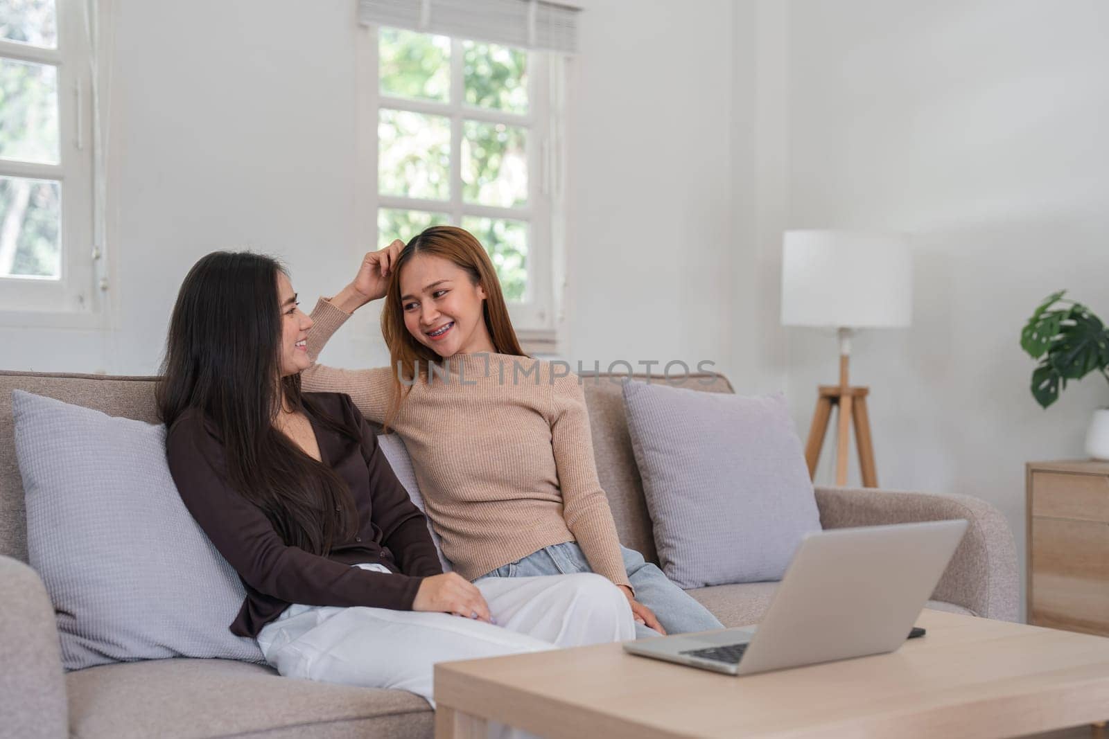 Lesbian couple sitting together on a sofa in a bright, modern living room, sharing a happy moment and smiling.